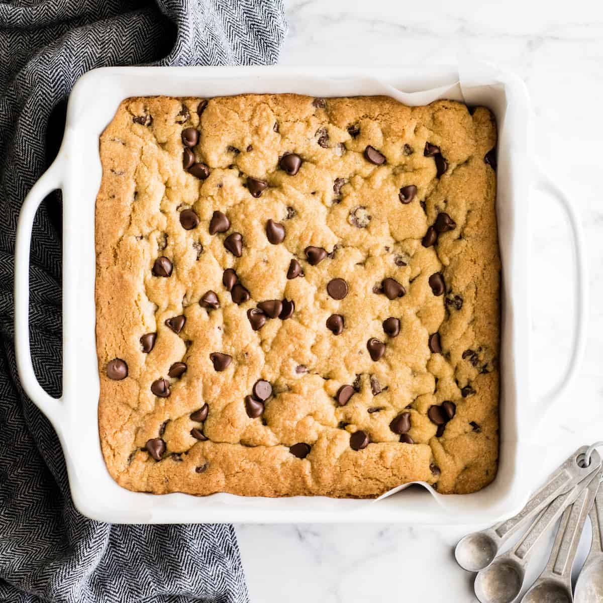 These are the absolute best chocolate chip cookie bars EVER. This cookie bar recipe is easy to make (5 minutes to mix, 20 minutes to bake) and results in a gooey, chewy, doughy yet fully cooked chocolate chip cookie bar that is 100% irresistible. Serve warm with a scoop of ice cream! #chocolatechipcookiebars #cookiebars #cookeis #dessert #baking overhead view of chocolate chip cookie bars baked in a square dish