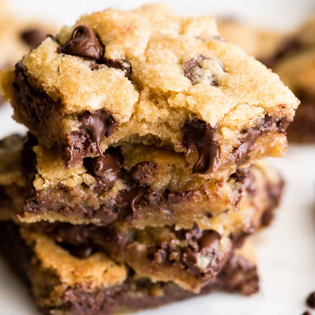 These are the absolute best chocolate chip cookie bars EVER. This cookie bar recipe is easy to make (5 minutes to mix, 20 minutes to bake) and results in a gooey, chewy, doughy yet fully cooked chocolate chip cookie bar that is 100% irresistible. Serve warm with a scoop of ice cream! #chocolatechipcookiebars #cookiebars #cookeis #dessert #baking front view of a stack of 4 chocolate chip cookie bars.