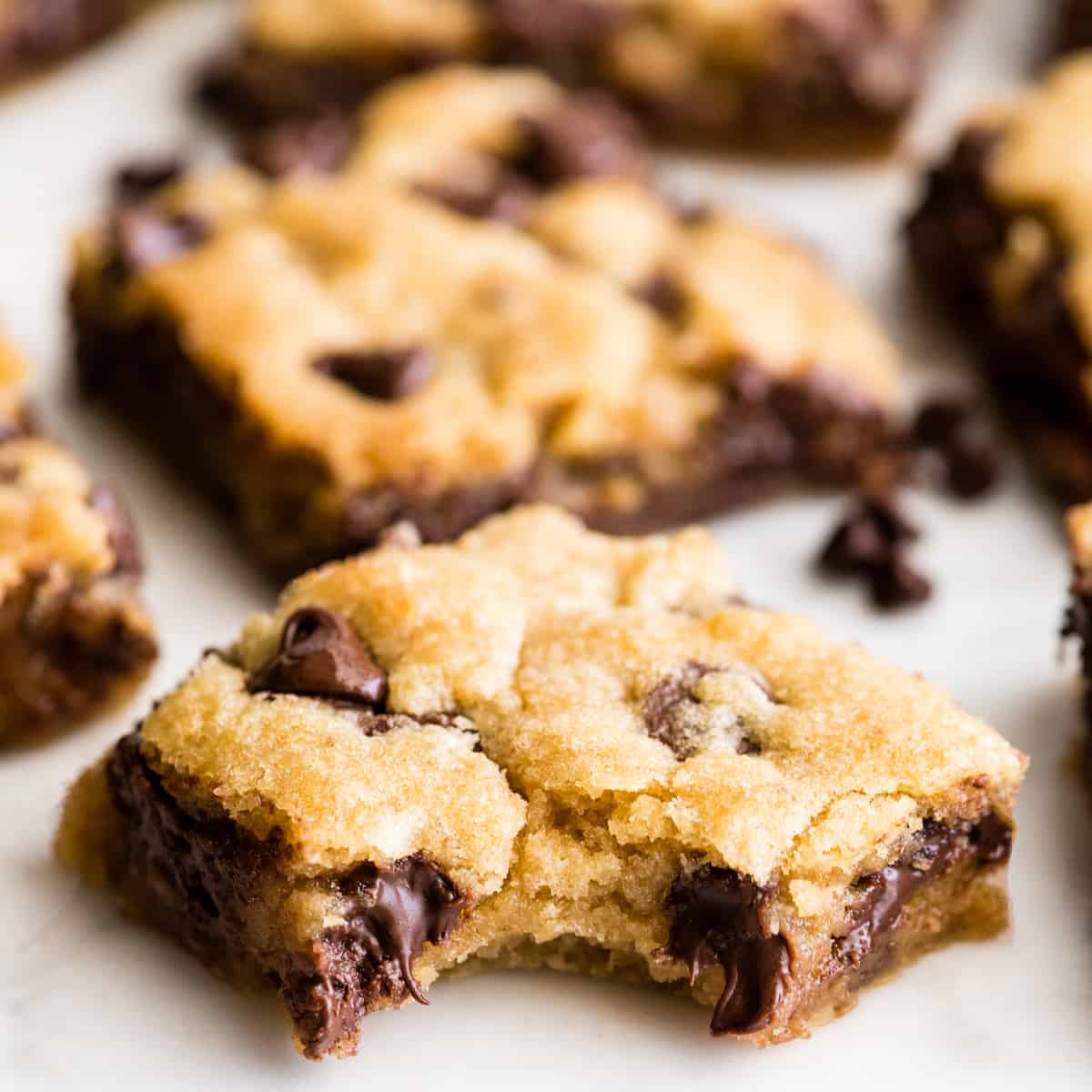 These are the absolute best chocolate chip cookie bars EVER. This cookie bar recipe is easy to make (5 minutes to mix, 20 minutes to bake) and results in a gooey, chewy, doughy yet fully cooked chocolate chip cookie bar that is 100% irresistible. Serve warm with a scoop of ice cream! #chocolatechipcookiebars #cookiebars #cookeis #dessert #baking front view of a chocolate chip cookie bar with a bite taken out of it