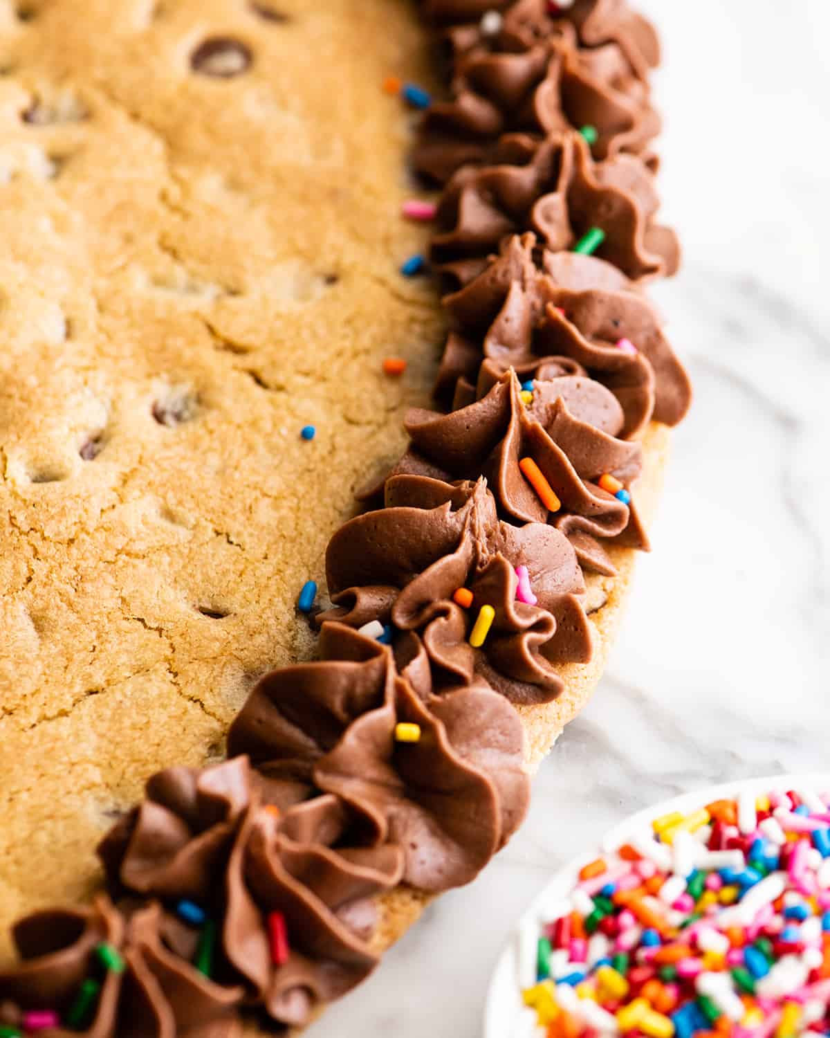 This chocolate chip cookie cake recipe is soft, chewy, slightly doughy and decorated with the best chocolate buttercream frosting. It's easy to make, large enough to feed a crowd, and even better than store-bought! overhead view of chocolate frosting on a Chocolate Chip Cookie Cake
