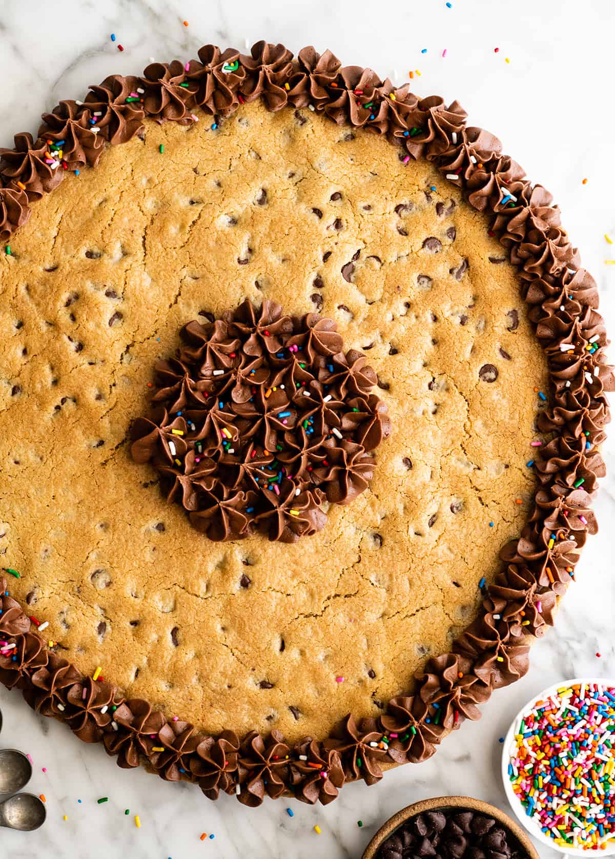 This chocolate chip cookie cake recipe is soft, chewy, slightly doughy and decorated with the best chocolate buttercream frosting. It's easy to make, large enough to feed a crowd, and even better than store-bought! overhead view of a Chocolate Chip Cookie Cake with chocolate frosting