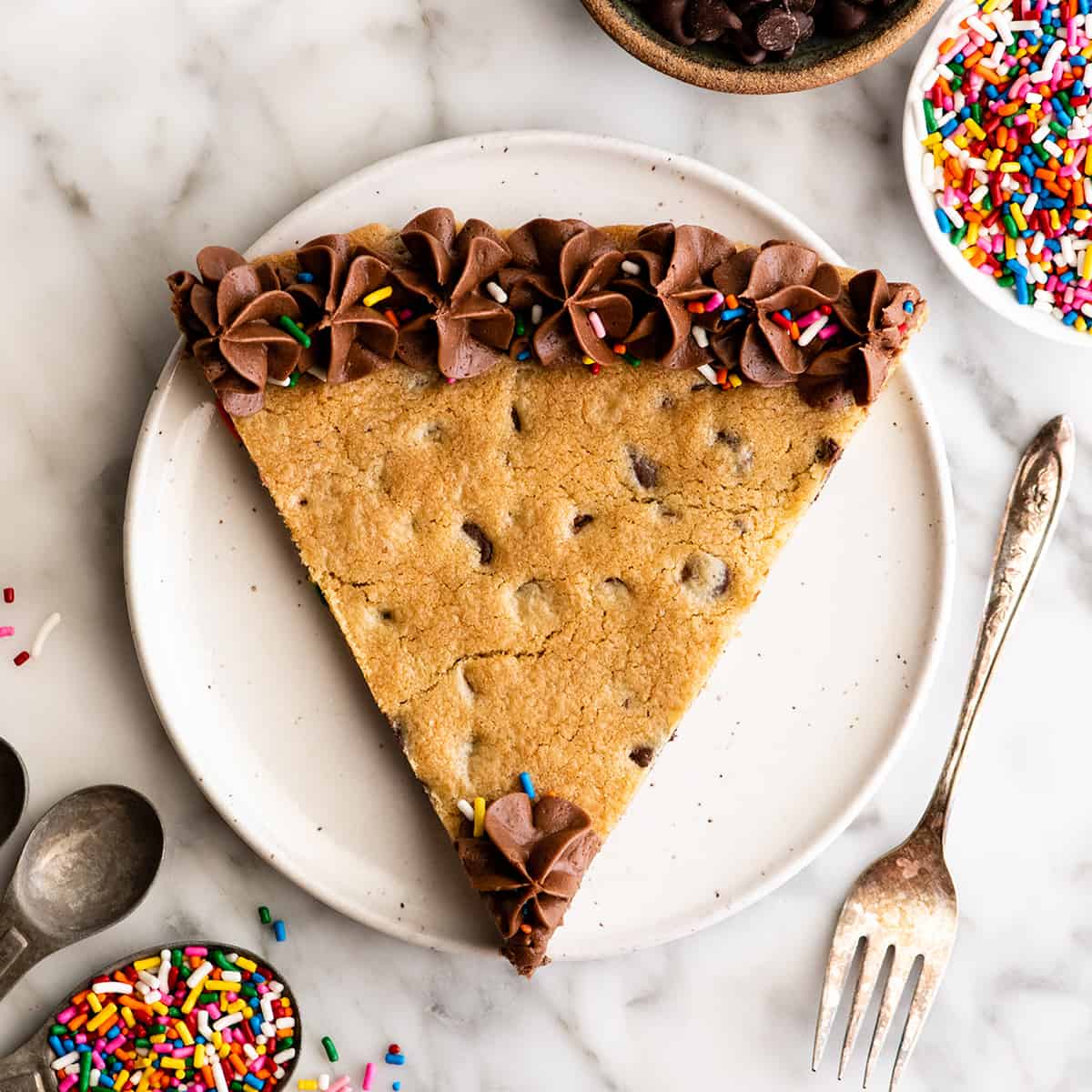 This chocolate chip cookie cake recipe is soft, chewy, slightly doughy and decorated with the best chocolate buttercream frosting. It's easy to make, large enough to feed a crowd, and even better than store-bought! overhead view of a pice of Chocolate Chip Cookie Cake Recipe