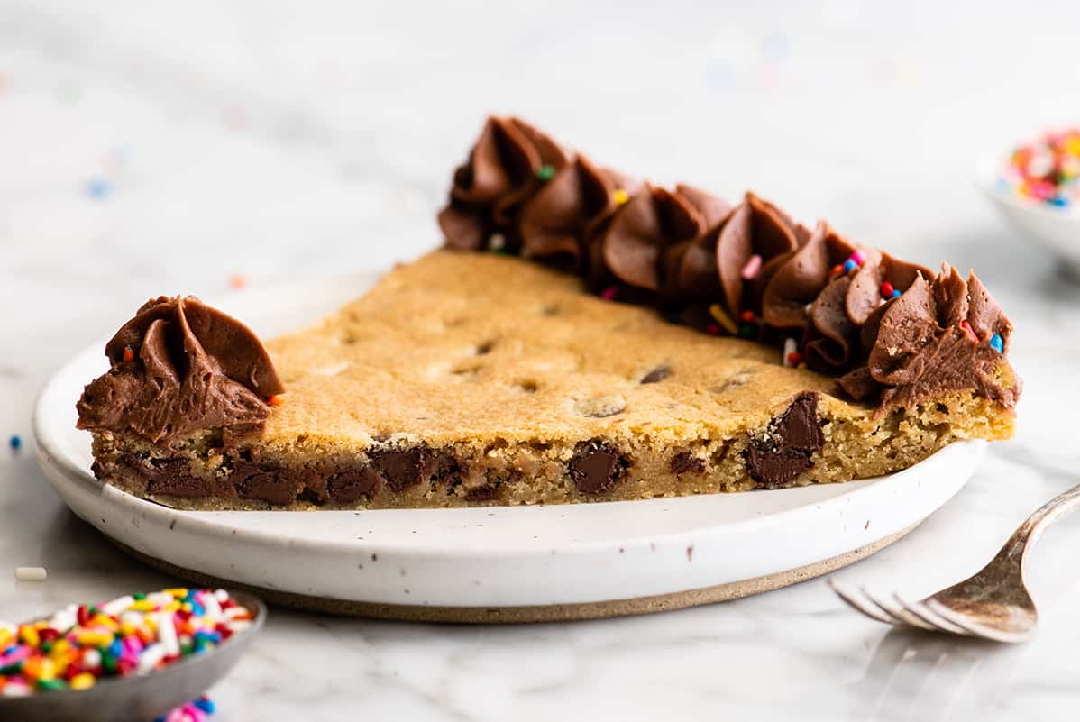This chocolate chip cookie cake recipe is soft, chewy, slightly doughy and decorated with the best chocolate buttercream frosting. It's easy to make, large enough to feed a crowd, and even better than store-bought! front view of a slice of this Chocolate Chip Cookie Cake Recipe