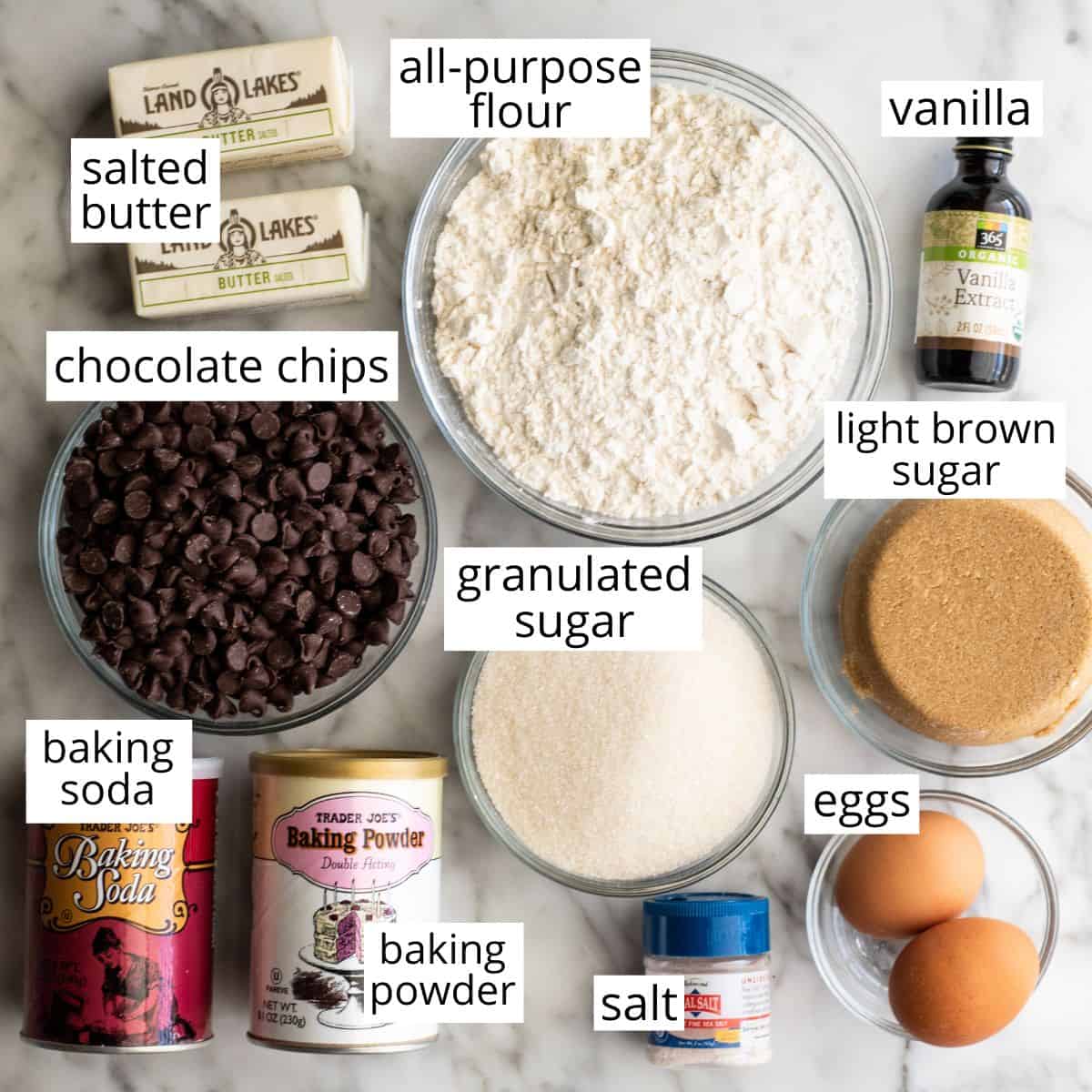 This chocolate chip cookie cake recipe is soft, chewy, slightly doughy and decorated with the best chocolate buttercream frosting. It's easy to make, large enough to feed a crowd, and even better than store-bought! overhead photo of the labeled ingredients in this Chocolate Chip Cookie Cake Recipe