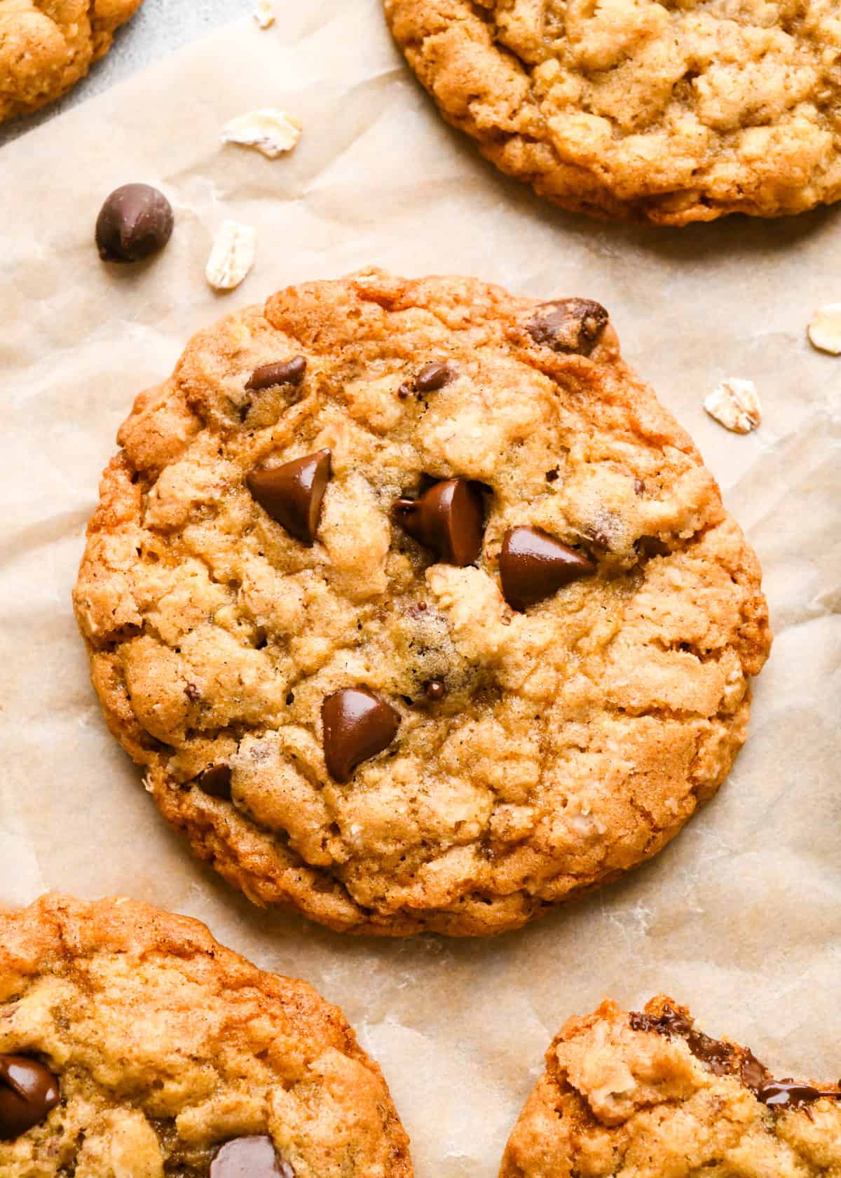 4 Oatmeal Chocolate Chip Cookies on parchment paper with raw oats and chocolate chips nearby