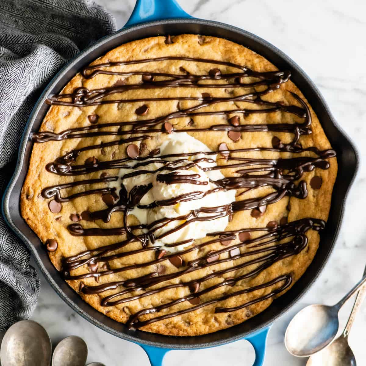 The BEST Chocolate Chip Skillet Cookie recipe! This ooey gooey, warm & melty skillet cookie (AKA: Pizookie) is completely irresistible. It's like eating warm cookie dough topped with vanilla ice cream, better than any restaurant version you've ever had! Plus it's easy to make & comes together in 20 minutes flat! #skilletcookie #pizookie #chocolatechipcookie #dessert #baking #joyfoodsunshine overhead view of a skillet cookie (pizookie) drizzled with chocolate topped with ice cream