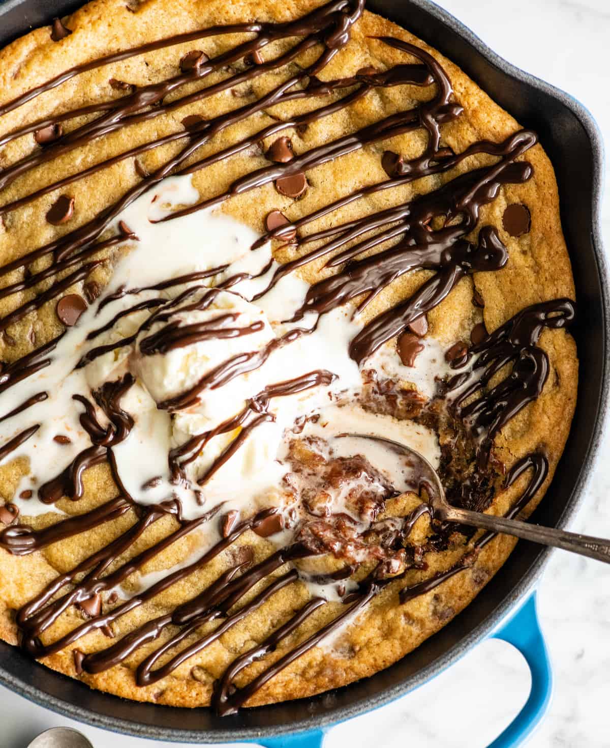 The BEST Chocolate Chip Skillet Cookie recipe! This ooey gooey, warm & melty skillet cookie (AKA: Pizookie) is completely irresistible. It's like eating warm cookie dough topped with vanilla ice cream, better than any restaurant version you've ever had! Plus it's easy to make & comes together in 20 minutes flat! #skilletcookie #pizookie #chocolatechipcookie #dessert #baking #joyfoodsunshine overhead view of a skillet cookie (pizookie) drizzled with chocolate topped with ice cream