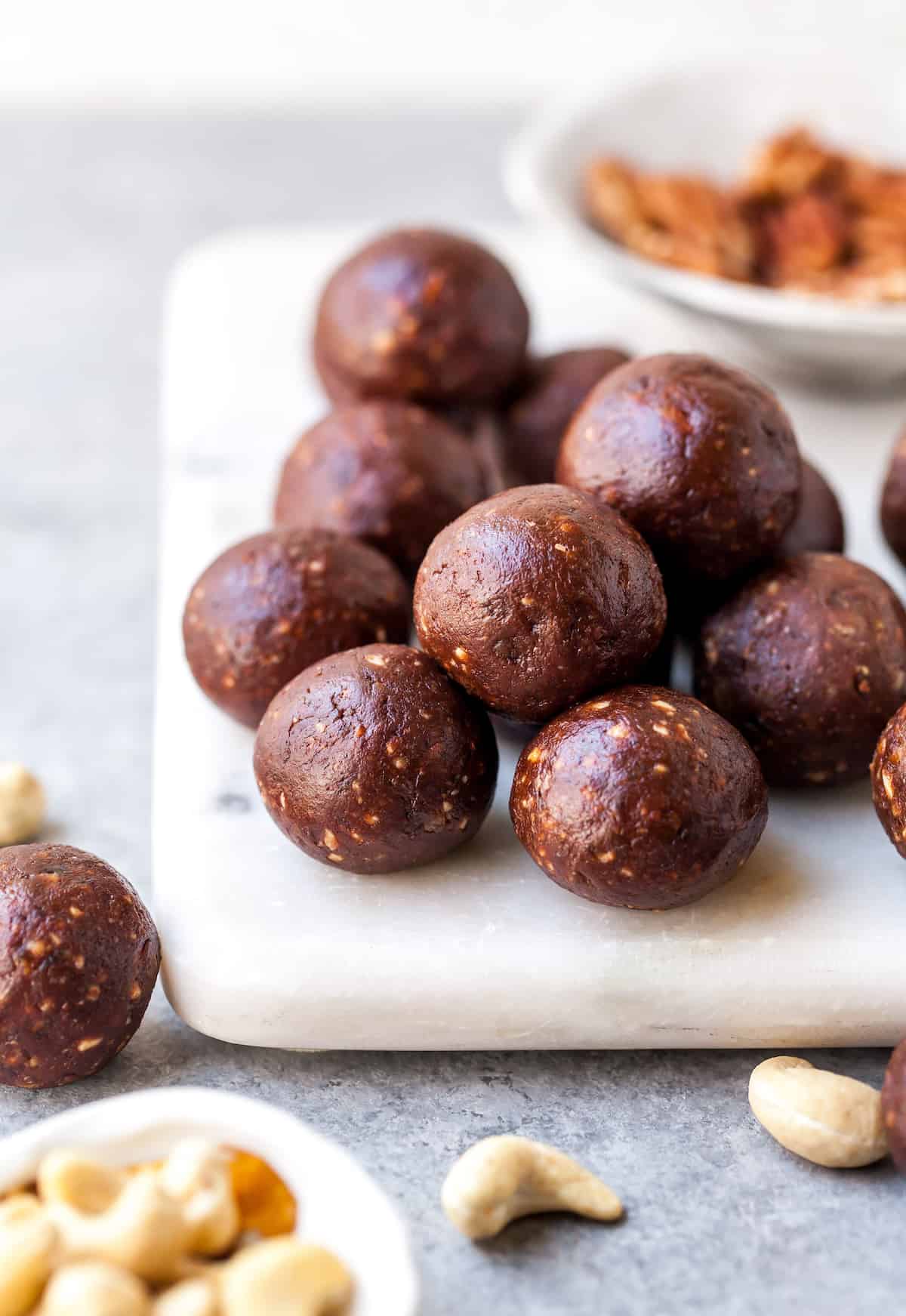No-Bake Chocolate Date Energy Balls Recipe! These healthy energy balls are made in 5 minutes with 8 ingredients and they taste brownie bites! They are vegan, Paleo gluten-free and have no refined sugar, but you'd never know it! They're also freezer-friendly! #energyballs #energybites #vegan #paleo #snack #glutenfree #joyfoodsunshine front view of chocolate date energy balls on a white serving board