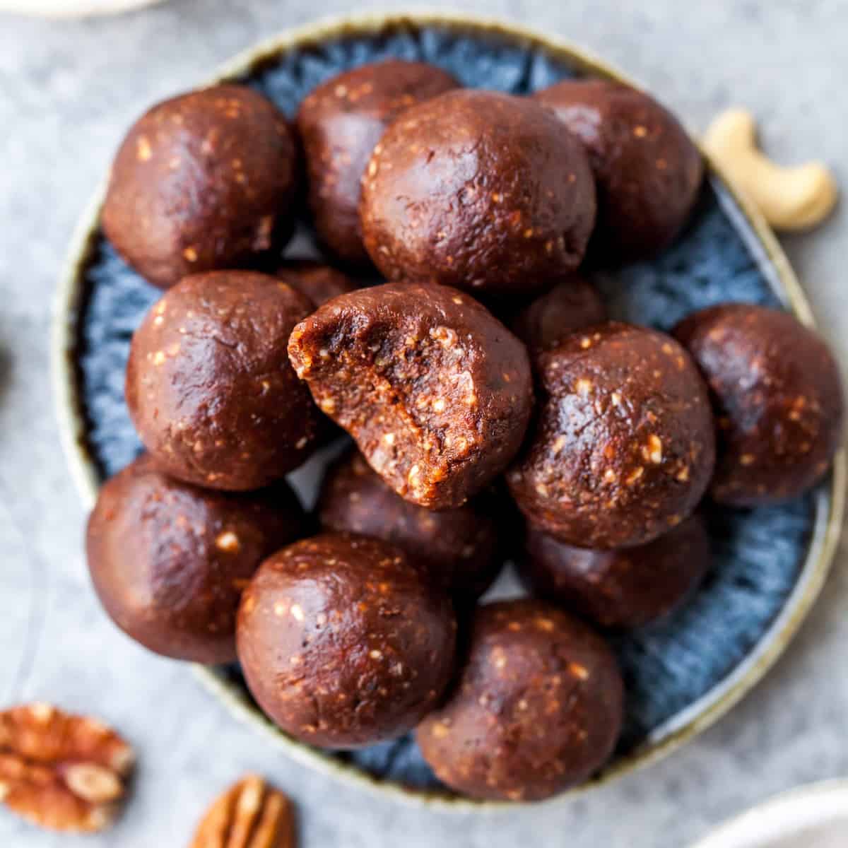 No-Bake Chocolate Date Energy Balls Recipe! These healthy energy balls are made in 5 minutes with 8 ingredients and they taste brownie bites! They are vegan, Paleo gluten-free and have no refined sugar, but you'd never know it! They're also freezer-friendly! #energyballs #energybites #vegan #paleo #snack #glutenfree #joyfoodsunshine Chocolate Date Energy Balls on a plate, one has a bite taken out of it