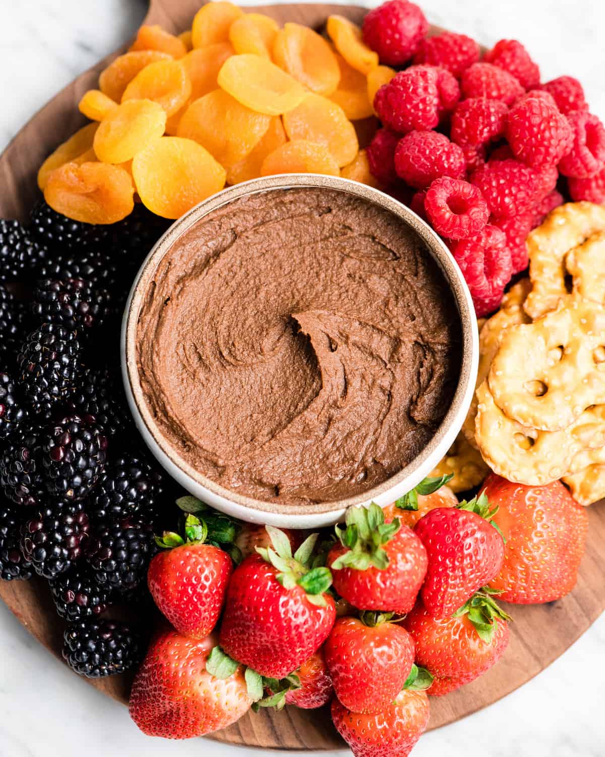 Healthy Chocolate Hummus Recipe is easy to make and ready in 5 minutes! It's a nutritious dip, appetizer, dessert, snack or spread that everyone in my family, including my kids, loves. This dessert hummus recipe is gluten-free, dairy-free, has no refined sugar & it's vegan! #hummus #chocolatehummus #vitamix #desserthummus #vegan Overhead view of a cheese board loaded with fruit, pretzels, etc. with a bowl of Chocolate Hummus in the middle