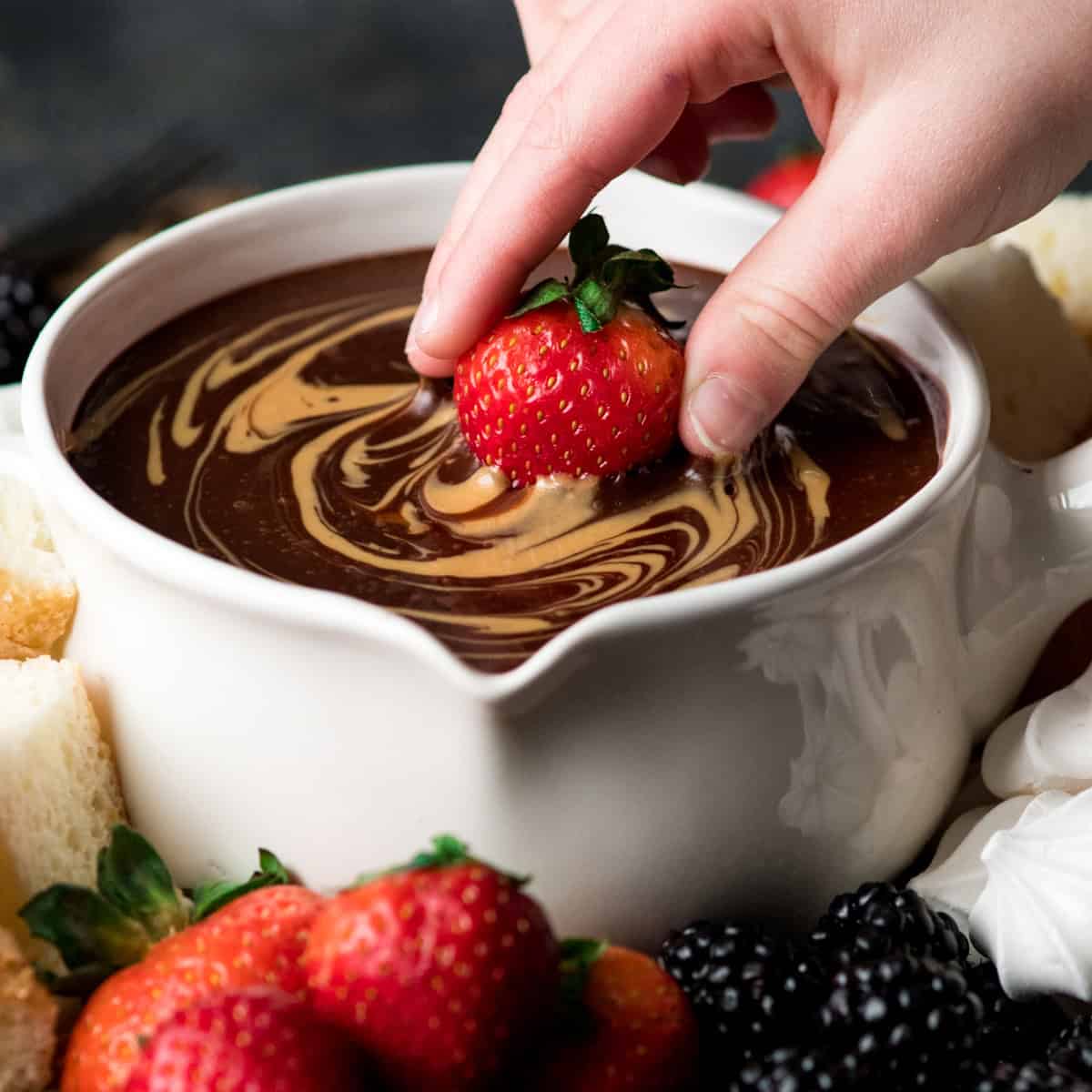 a strawberry being dipped into Chocolate Peanut Butter Fondue in a white fondue pot
