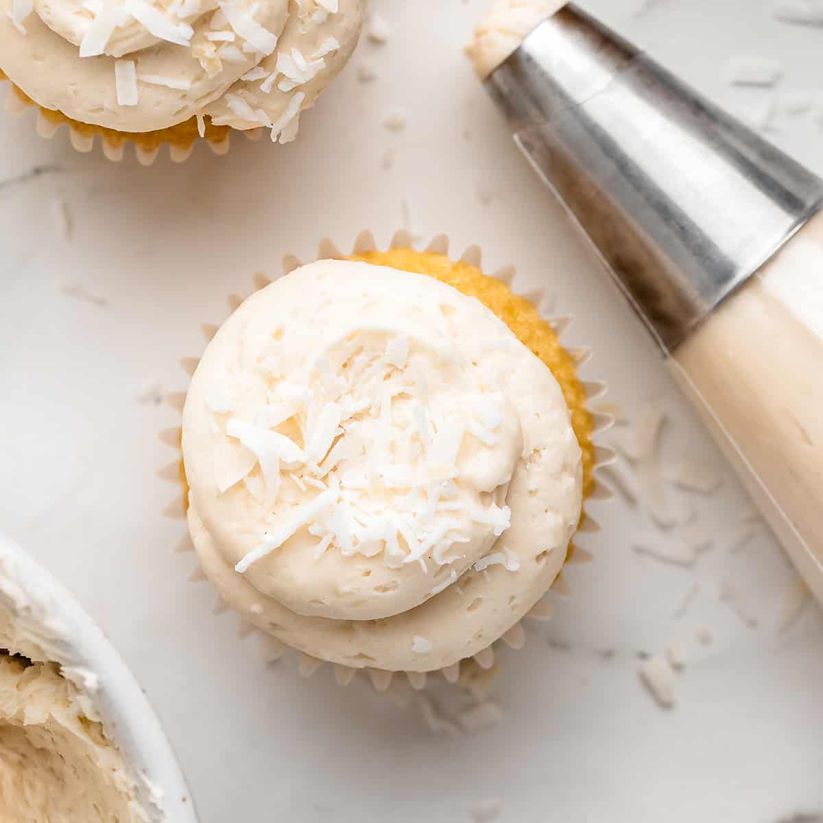 Coconut Frosting in a piping bag and piped on top of 2 cupcakes