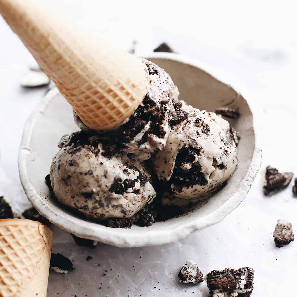 The best cookies and cream ice cream recipe! A creamy Oreo ice cream is loaded with crushed and chopped cookies for a big cookie flavor in every bite! Oreo ice cream in a bowl with an ice cream cone