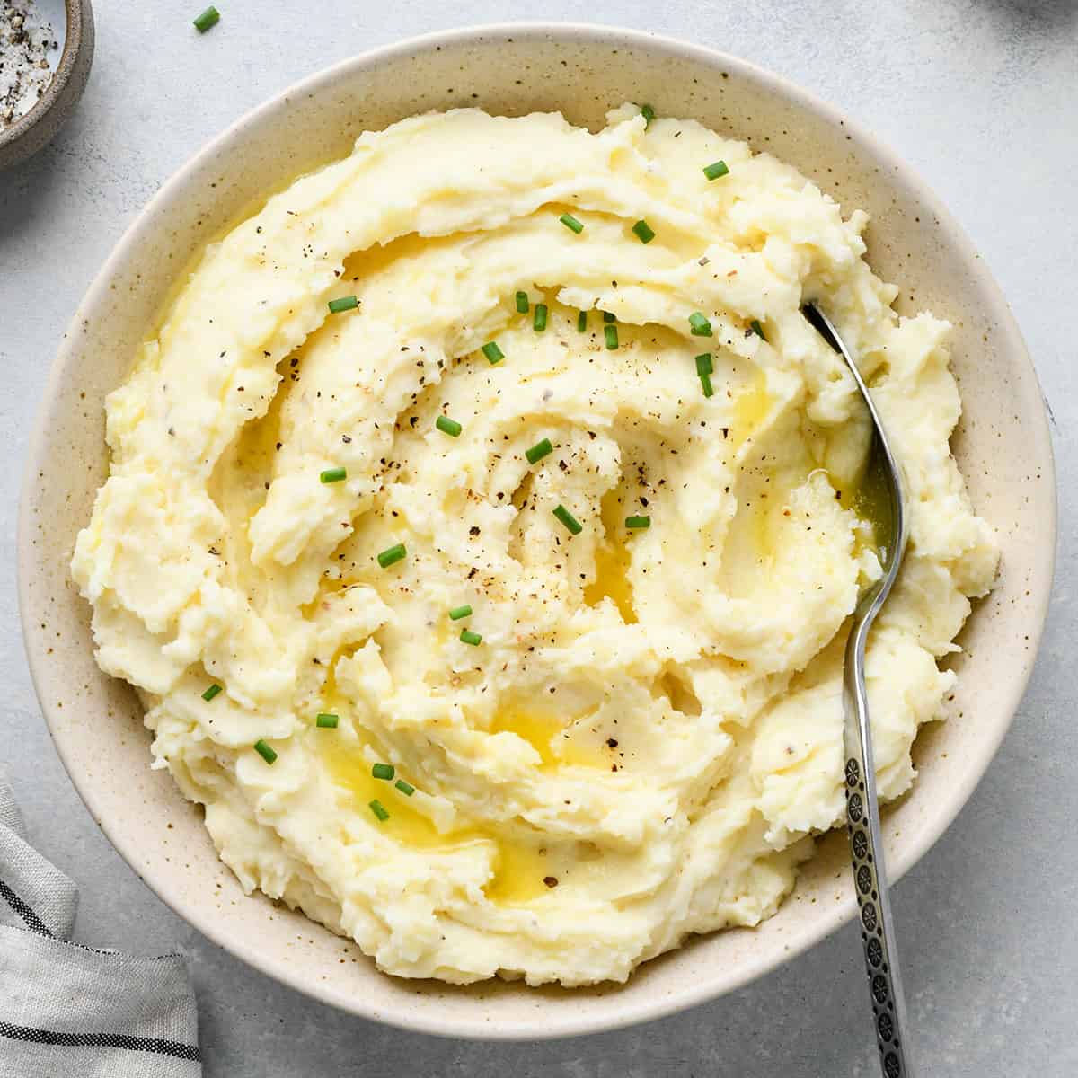 a bowl of Cream Cheese Mashed Potatoes with butter, chives, pepper and a spoon