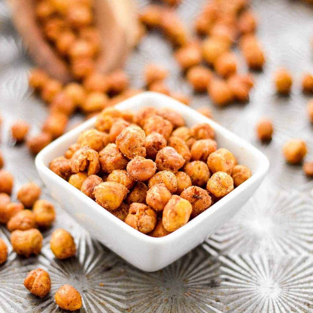 These perfectly seasoned Crunchy Roasted Chickpeas make a great snack or salad topper! They're easy, flavorful & healthy! Vegan, gluten-free, dairy-free, & sugar-free! #chickpeas #recipe #crunchy #roasted #snack #glutenfree #dairyfree #sugarfree #vegan #crunchychickepeas #healthy #healthyrecipe #recipe Side, close up shot of a small square dish full of crunchy roasted chickpeas