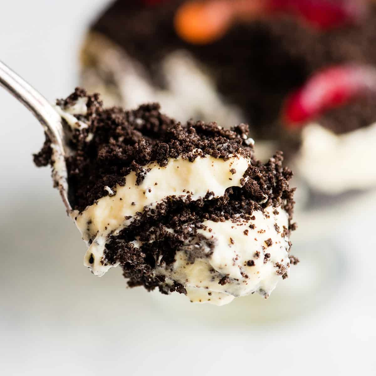 This Easy Dirt Cake Recipe (Oreo Dirt Pudding) is one of our favorite no-bake desserts! Crushed Oreos are layered between a french vanilla pudding mixture for a kid-friendly, make-ahead dessert recipe perfect for any potluck or BBQ! Add gummy worms for a whimsical touch! #dirtcake #dirtpudding #oreos #oreopudding #nobake #dessert #potluck #bbq #summer up-close front view of a spoon holding a scoop of Oreo Dirt Cake with two layers of pudding and two layers of crushed oreos