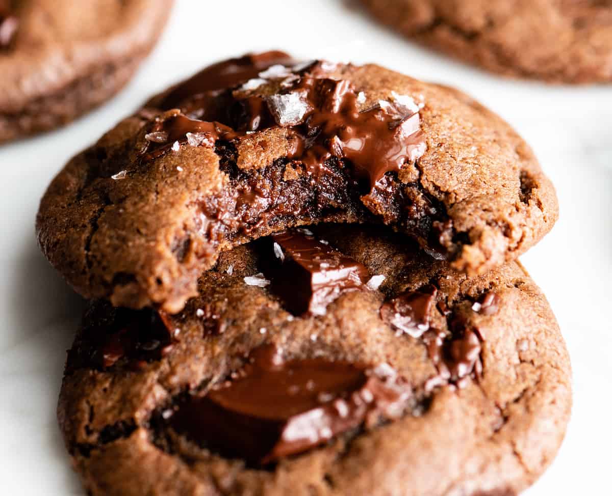 The BEST easy double chocolate chip cookie recipe ever! These chocolate cookies have soft centers, chewy edges and are irresistibly chocolatey. They come together in 5 minutes and require only 30 minutes of chilling time! #chocolate #cookies #chocolatecookies #baking #joyfoodsunshine front view of two chocolate cookies, one with a bite taken out