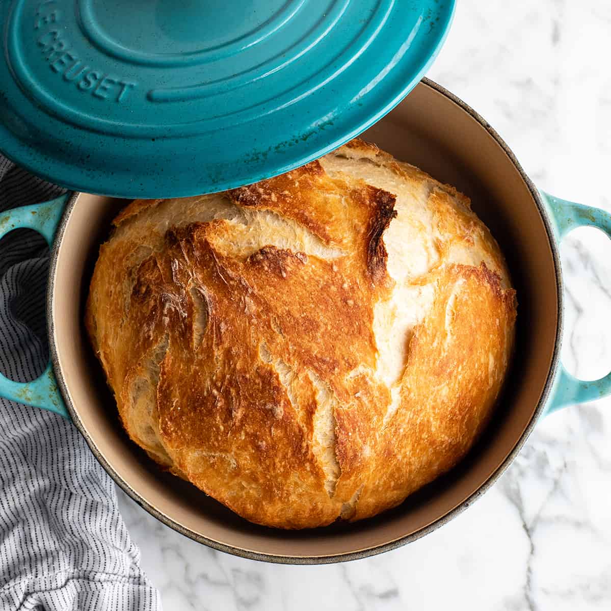 Easy Dutch Oven No Knead Bread recipe is made with only 4 ingredients and takes 5 minutes of prep time! If you want to make delicious homemade bread that looks & tastes like it came from a fancy bakery but actually takes very little effort, this dutch oven bread recipe is for you! overhead view of baked dutch oven bread in a blue dutch oven