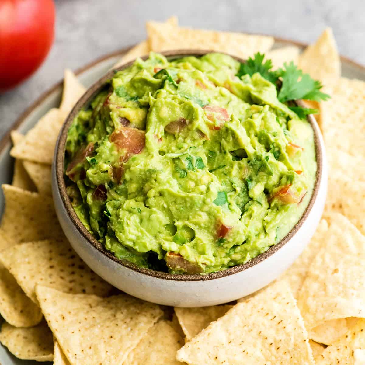 This quick & easy guacamole recipe is made with a handful of healthy ingredients and is ready in 5 minutes! This simple guacamole dip is our favorite appetizer and we always make it on taco nights! Watch the video to learn how to make this guacamole recipe! #guacamole #guacamolerecipe #tacos #appetizer #dip a bowl of homemade guacamole surrounded by chips