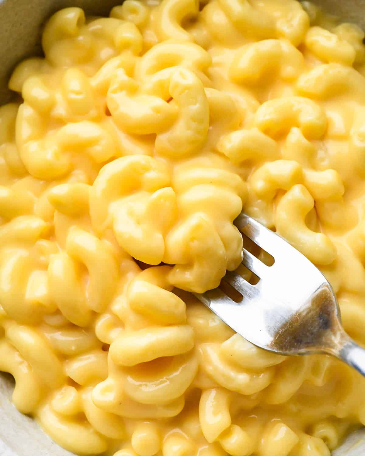 This Easy Homemade Mac and Cheese Recipe is made with 8 ingredients in 15 minutes on the stovetop (no baking required)! Time to ditch the boxed mac and cheese for this irresistibly creamy, smooth & cheesy homemade recipe! #homemade #macandcheese #homemademacandcheese #sidedish #maindish #kidfriendly a fork taking a bite of mac and cheese in a bowl