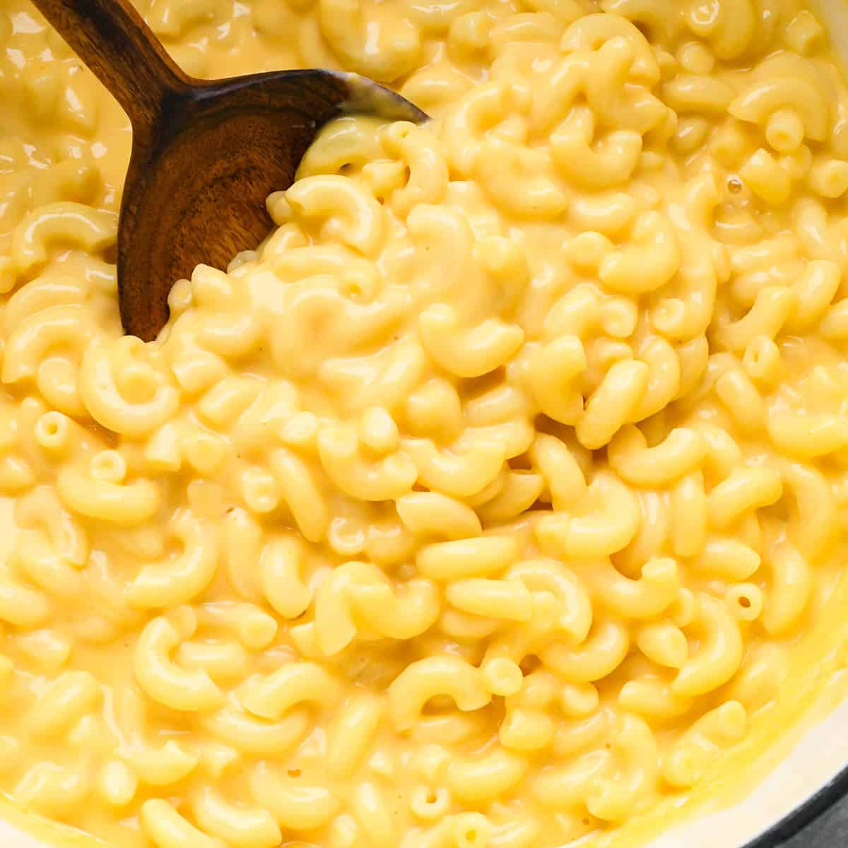 This Easy Homemade Mac and Cheese Recipe is made with 8 ingredients in 15 minutes on the stovetop (no baking required)! Time to ditch the boxed mac and cheese for this irresistibly creamy, smooth & cheesy homemade recipe! #homemade #macandcheese #homemademacandcheese #sidedish #maindish #kidfriendly overhead photo of homemade mac and cheese in a pot with a spoon taking a scoop