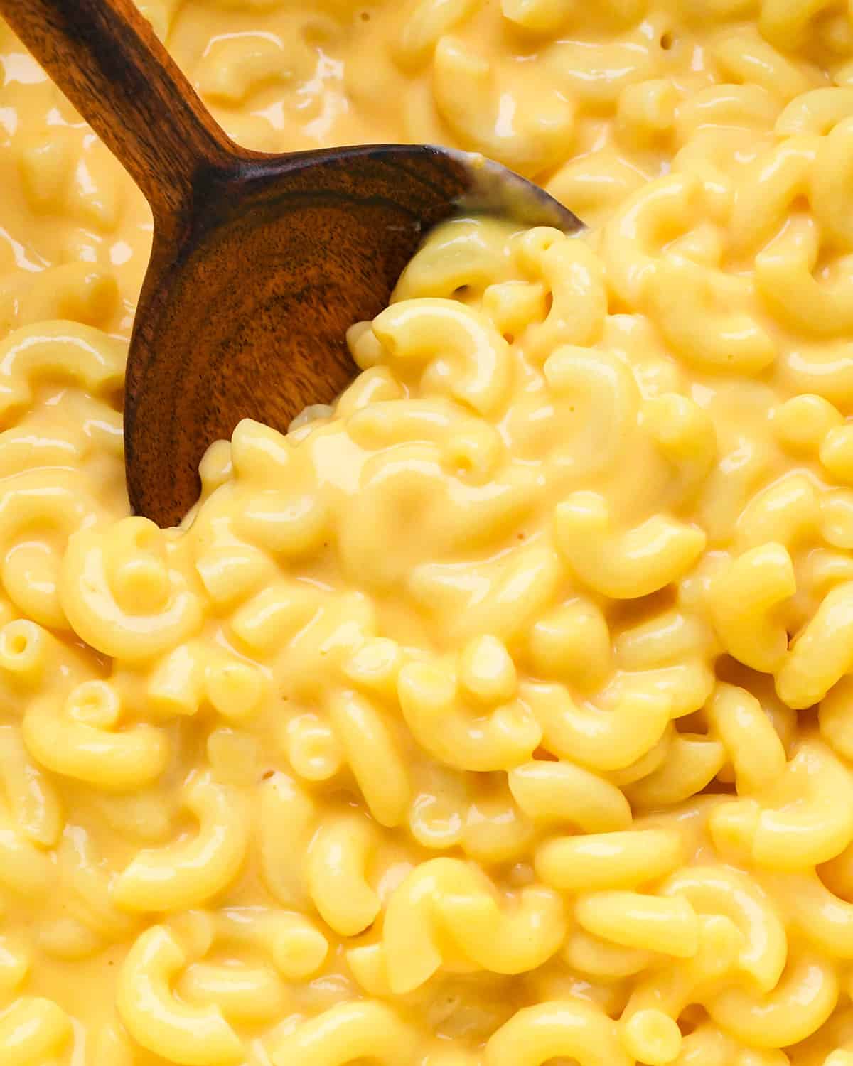 This Easy Homemade Mac and Cheese Recipe is made with 6 ingredients in 15 minutes on the stovetop (no baking required)! Time to ditch the boxed mac and cheese for this irresistibly creamy, smooth & cheesy homemade recipe! #homemade #macandcheese #homemademacandcheese #sidedish #maindish #kidfriendly overhead view of Homemade Mac and Cheese in a pot with a spoon taking a scoop