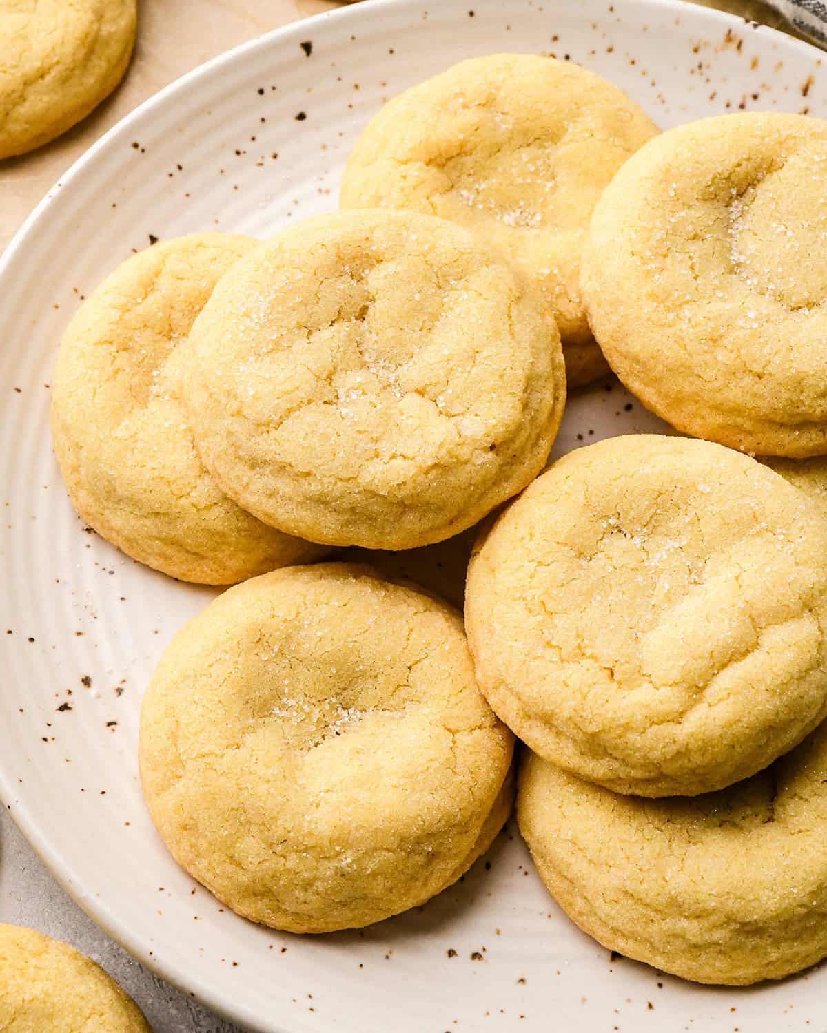 7 easy sugar cookies on a plate sprinkled with granulated sugar with other cookies around the plate