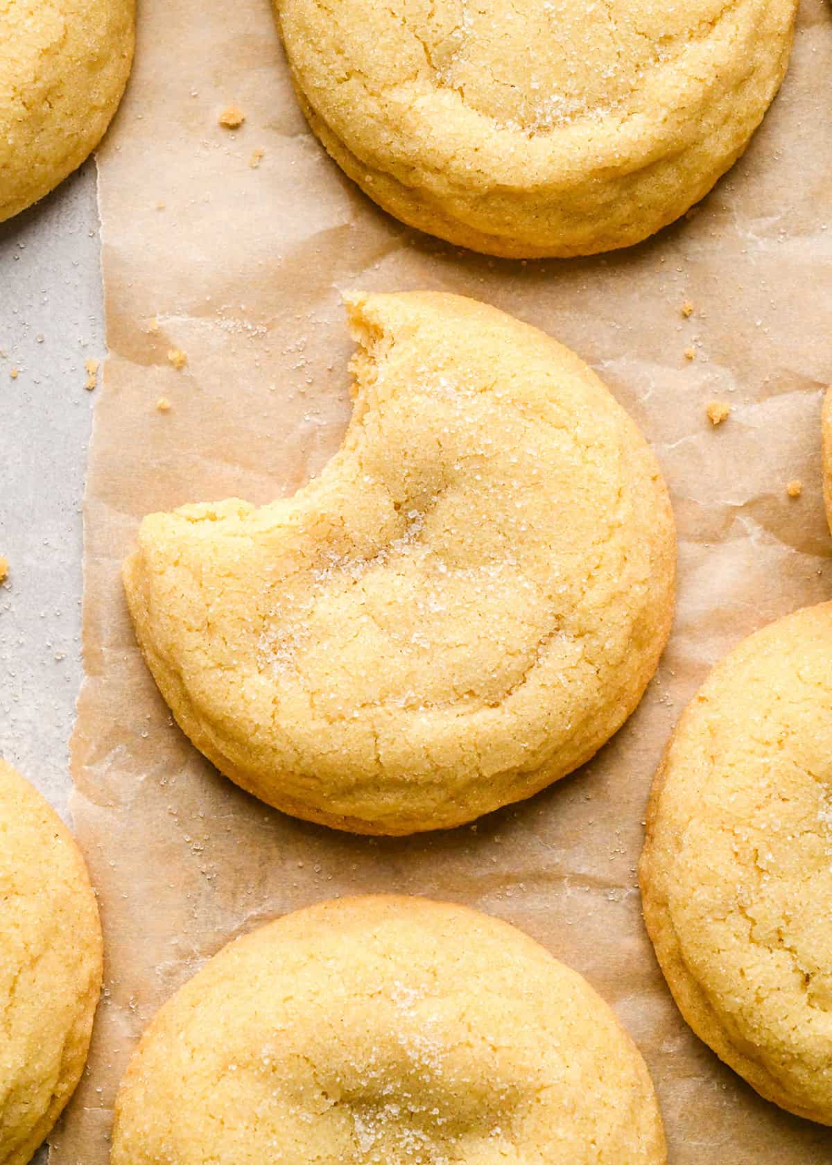 5 Easy Sugar Cookies on parchment paper rolled in granulated sugar, the largest one in the middle has a bite taken out of it