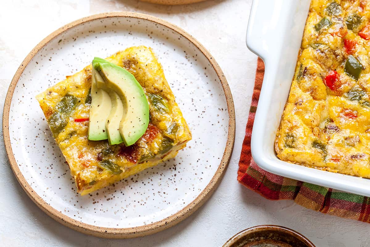 This Egg Casserole (Egg Bake) is an easy breakfast casserole that's made with only 9 ingredients (eggs, veggies, bacon, cheese and seasoning)! It's a healthy, low-carb way to start the day! #eggcasserole #breakfastcasserole #bacon #eggs #breakfast #brunch #recipe #joyfoodsunshine overhead view of a slice of egg casserole next to the baking dish of egg bake