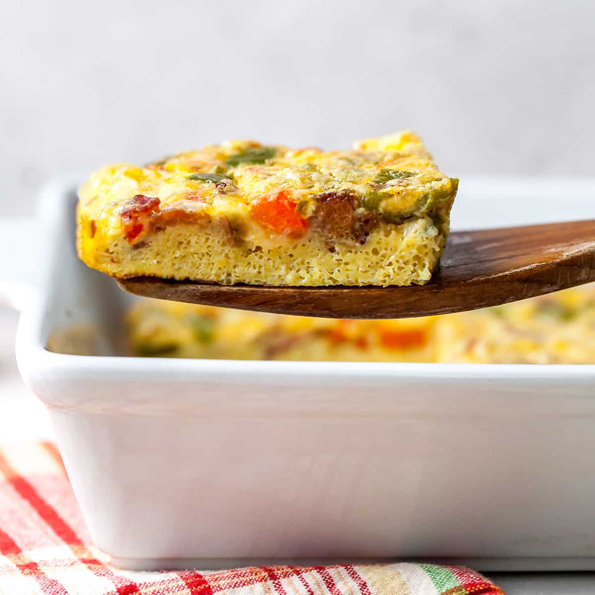 front view of a piece of egg casserole being lifted out of the baking dish with a wooden spatula