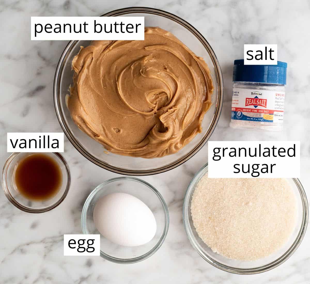 These Flourless Peanut Butter Cookies are easy to make with 4 ingredients in 15 minutes! These gluten-free peanut butter cookies are so good no one can tell they're made without flour or butter! overhead view of the labeled ingredients in this flourless peanut butter cookie recipe