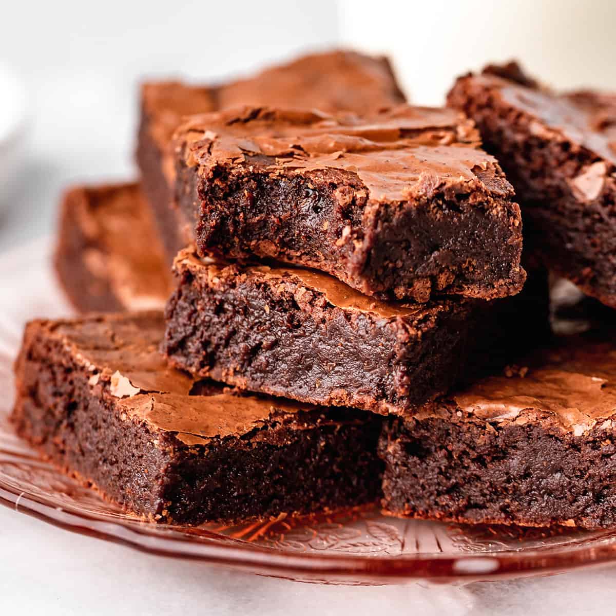 This is the best brownie recipe EVER! These fudgy brownies are homemade from scratch and have a gorgeous crinkly top with a gooey middle! They're easy to make with only 7 ingredients! Ditch the box and make these today! #brownies #brownierecipe #homemadebrownies #fudgybrownies #dessert #browniesfromscratch #baking #dessert #chocolate 7 brownies stacked on a plate, one has a bite taken out of it