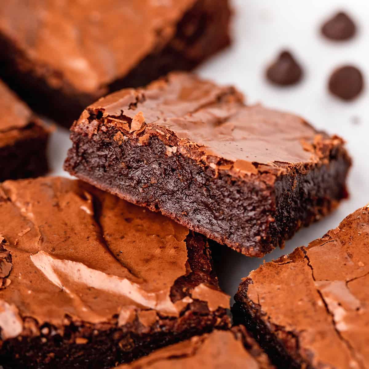 This is the best brownie recipe EVER! These fudgy brownies are homemade from scratch and have a gorgeous crinkly top with a gooey middle! They're easy to make with only 7 ingredients! Ditch the box and make these today! #brownies #brownierecipe #homemadebrownies #fudgybrownies #dessert #browniesfromscratch #baking #dessert #chocolate 4 brownies, one resting on top of another so the inside is visible