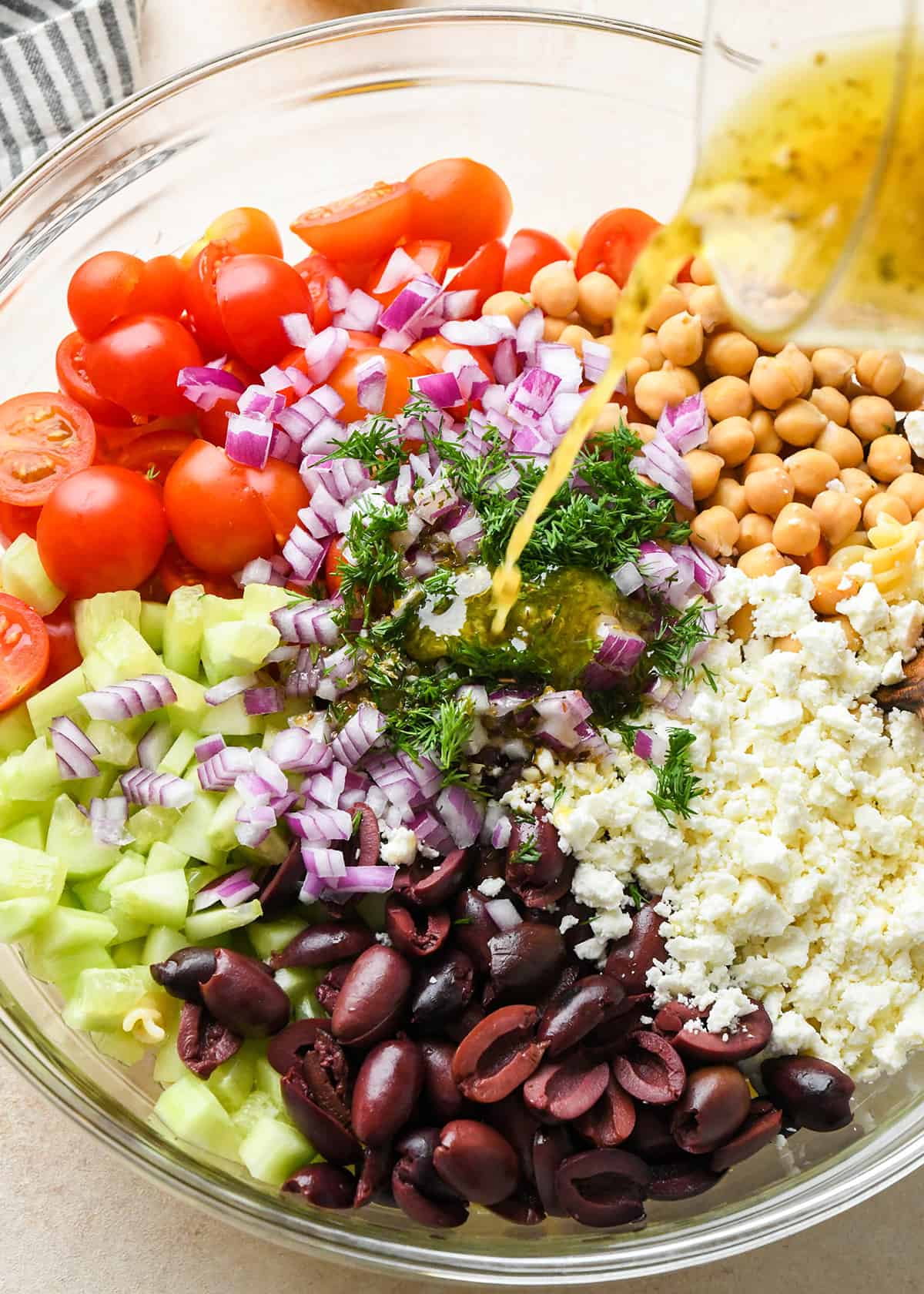dressing being poured over greek pasta salad ingredients