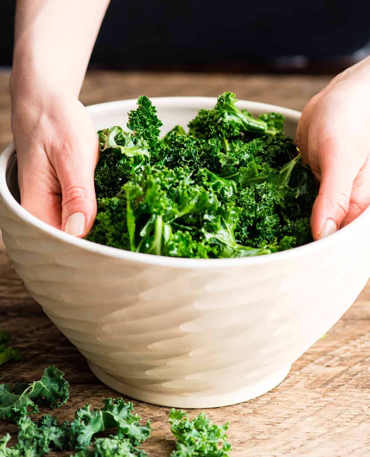 This is the best Baked Kale Chips recipe ever! Homemade crispy kale chips are a delicious, healthy snack made with only five ingredients. Roasting kale chips in the oven keeps them crispy for days! Hands in a bowl massaging olive oil into kale leaves showing how to make kale chips