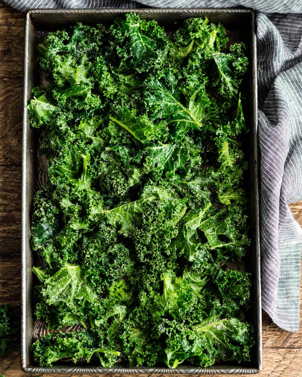 This is the best Baked Kale Chips recipe ever! Homemade crispy kale chips are a delicious, healthy snack made with only five ingredients. Roasting kale chips in the oven keeps them crispy for days! overhead photo showing how to make kale chips