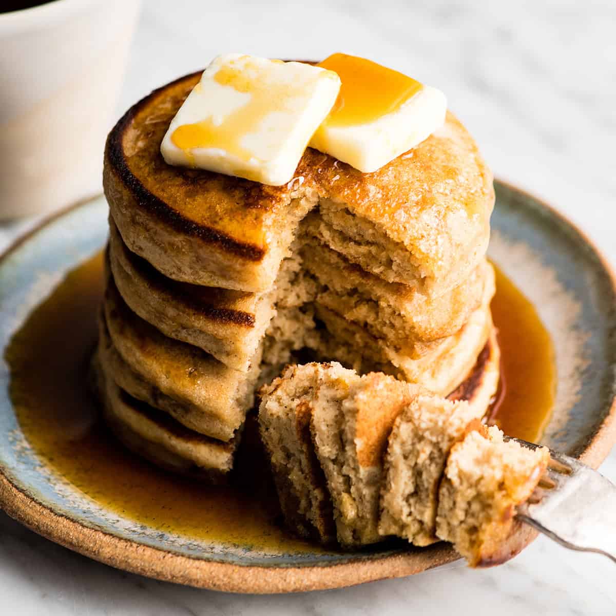 a stack of 4 Greek Yogurt Pancakes with butter and syrup. A bite is cut out of the stack on a fork on the plate.