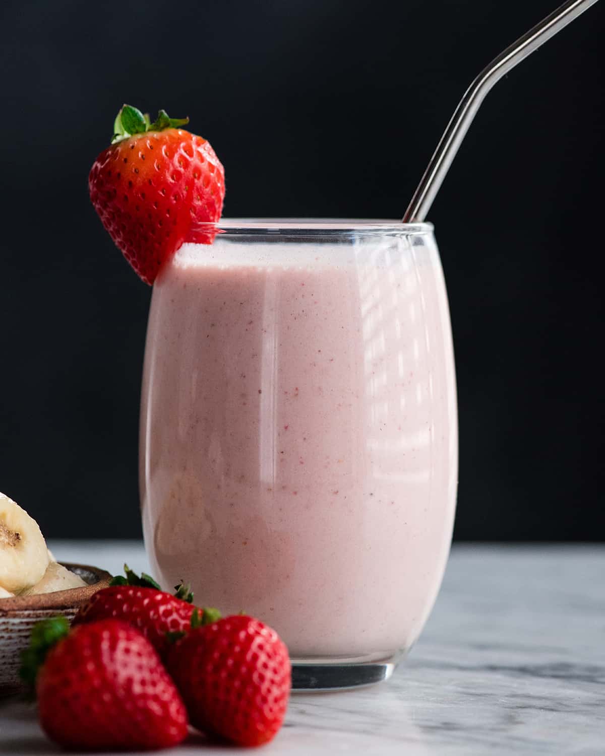 The BEST strawberry banana smoothie recipe ever! It's easy (ready in less than 5 minutes), healthy, and made with yogurt so it's full of protein! It's the perfect snack or breakfast! #smoothie #strawberrybananasmoothie #strawberry #banana #breakfast #snack #vitamix a glass filled with strawberry banana smoothie with a straw and strawberries.