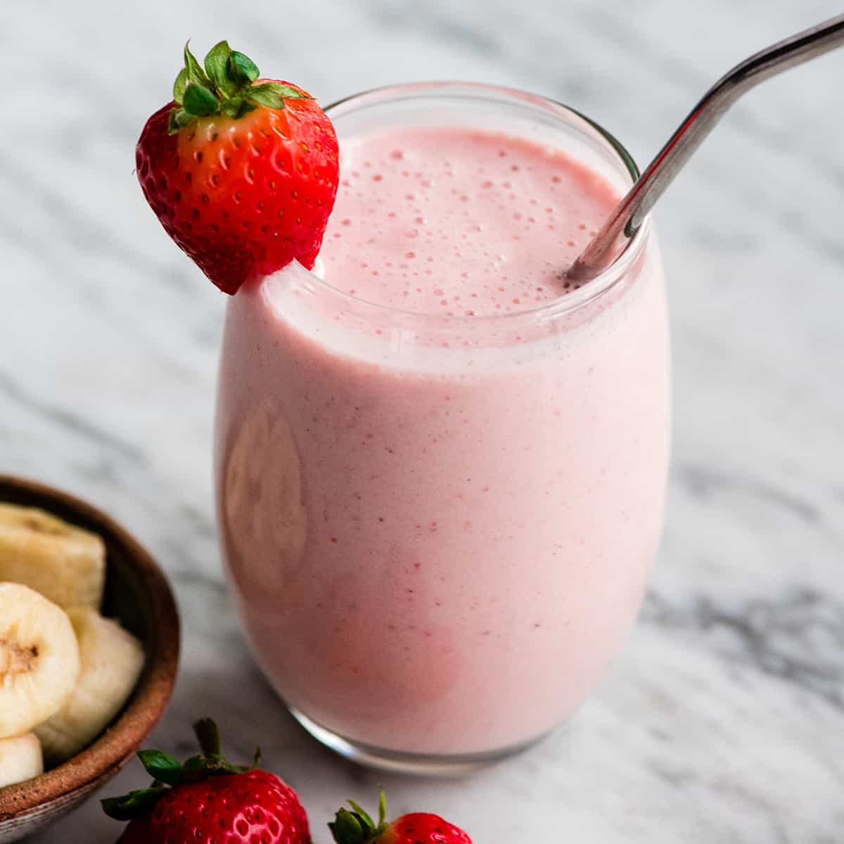The BEST strawberry banana smoothie recipe ever! It's easy (ready in less than 5 minutes), healthy, and made with yogurt so it's full of protein! It's the perfect snack or breakfast! #smoothie #strawberrybananasmoothie #strawberry #banana #breakfast #snack #vitamix a glass filled with strawberry banana smoothie with a straw and strawberries.