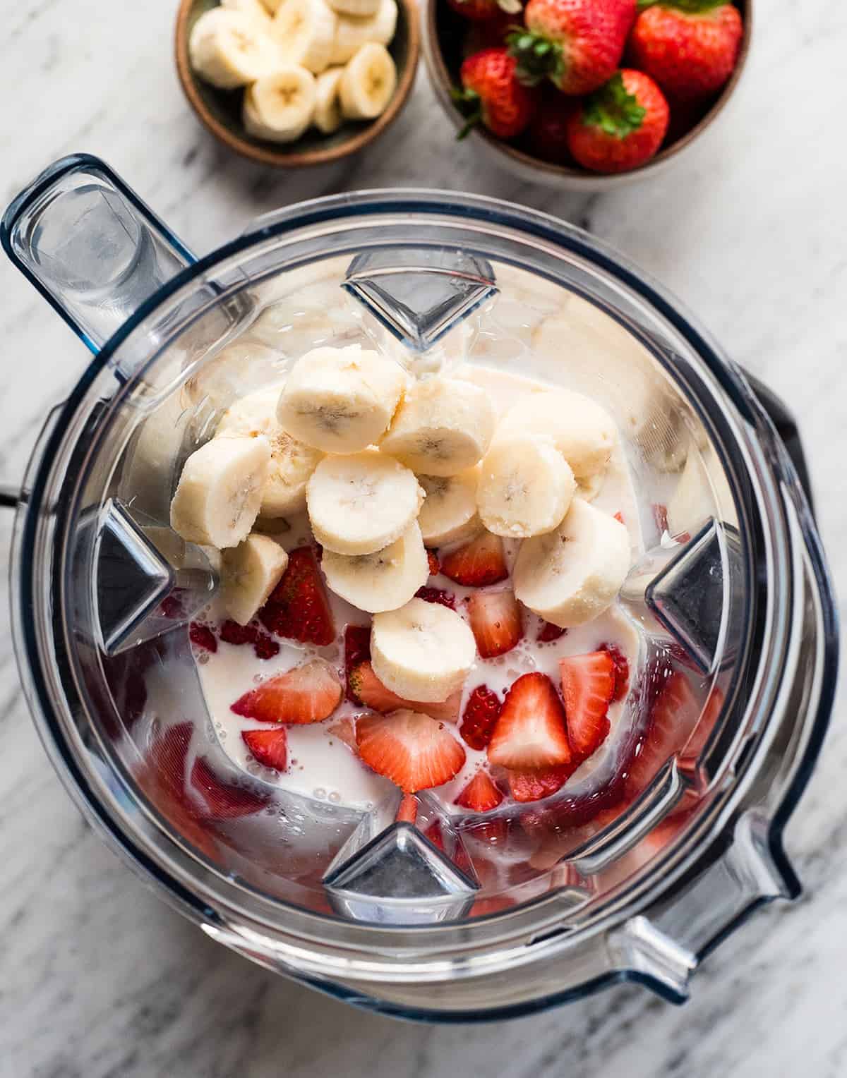 The BEST strawberry banana smoothie recipe ever! It's easy (ready in less than 5 minutes), healthy, and made with yogurt so it's full of protein! It's the perfect snack or breakfast! #smoothie #strawberrybananasmoothie #strawberry #banana #breakfast #snack #vitamix overhead view of the ingredients in this strawberry banana smoothie recipe in the vitamix before blending
