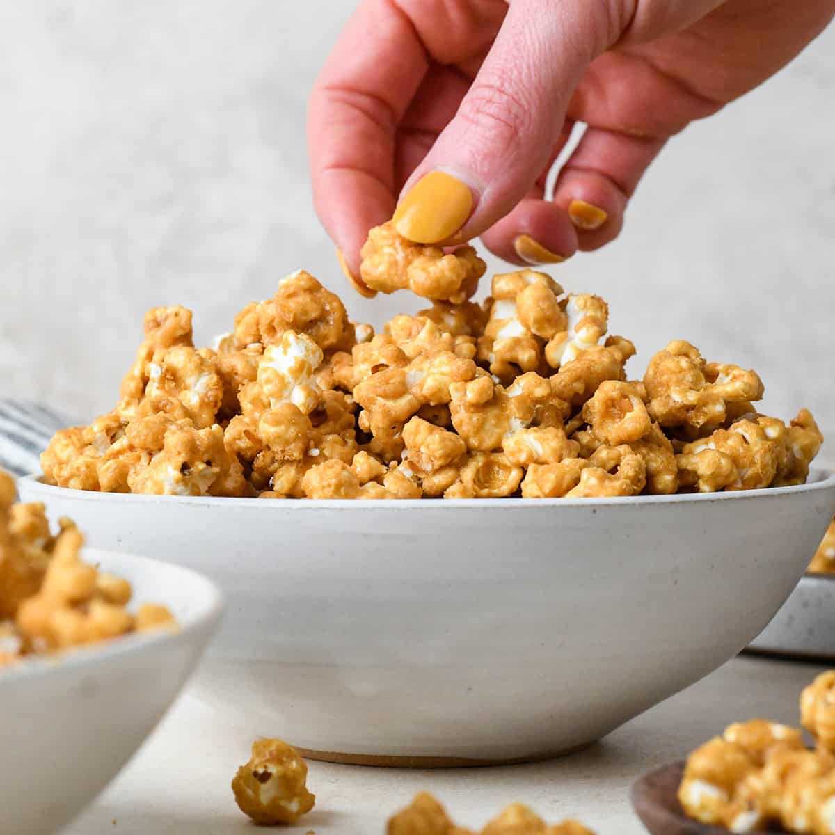 a hand taking a piece of caramel popcorn out of a large bowl of caramel corn.