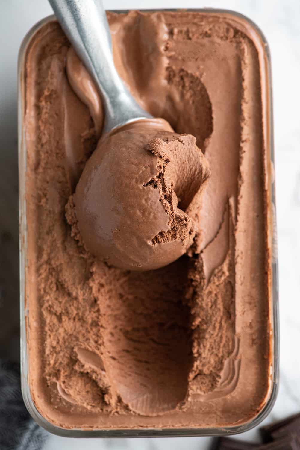 Rich, ultra-creamy, and chocolatey, this is the best homemade chocolate ice cream recipe ever! It's easy to make with only 7 ingredients (including two forms of chocolate), has a rich chocolate flavor, and is just as good as any ice cream shop! Overhead photo of an ice cream scoop scooping some chocolate ice cream out of a glass storage container