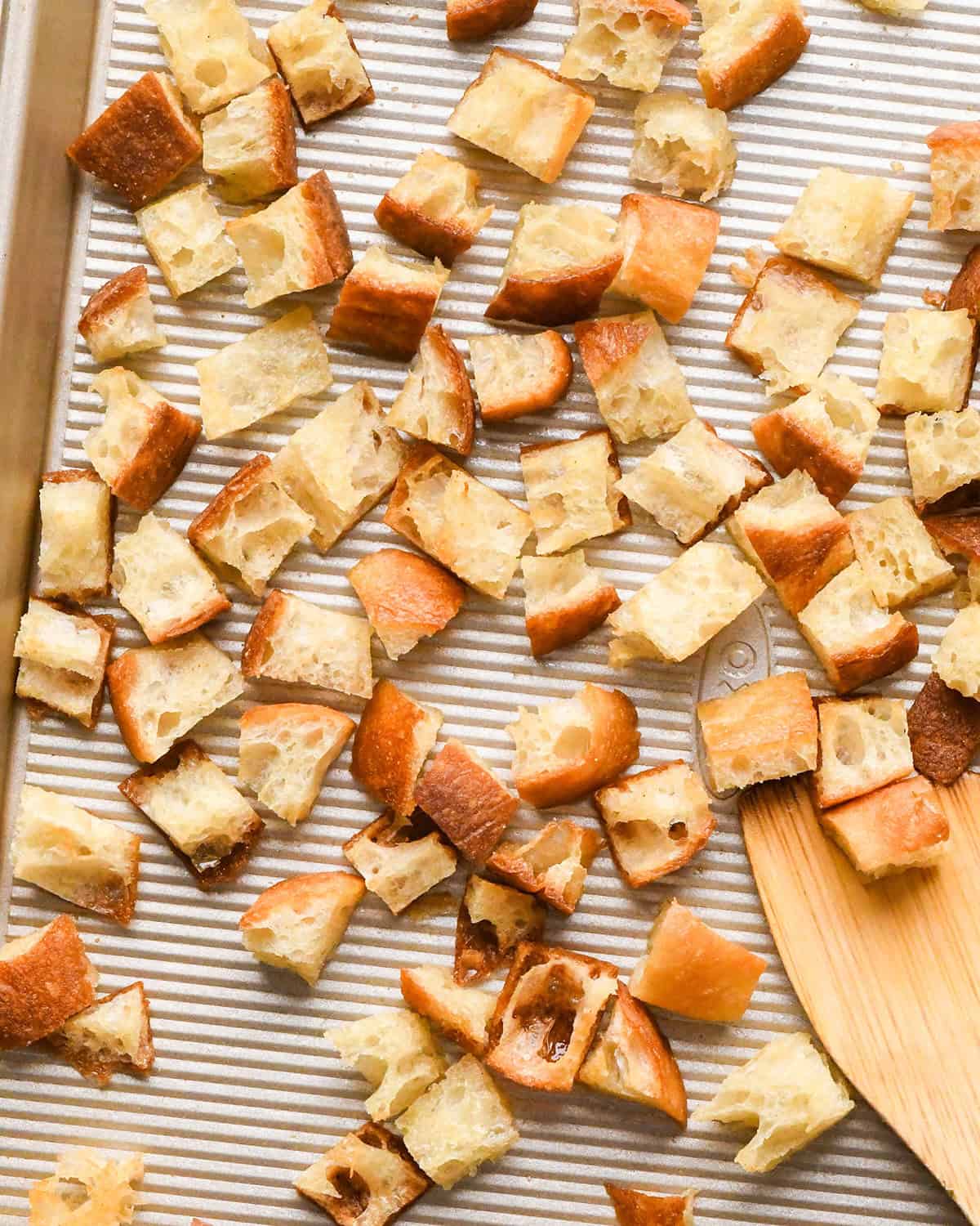 Homemade Croutons on a baking sheet with a wooden spatula