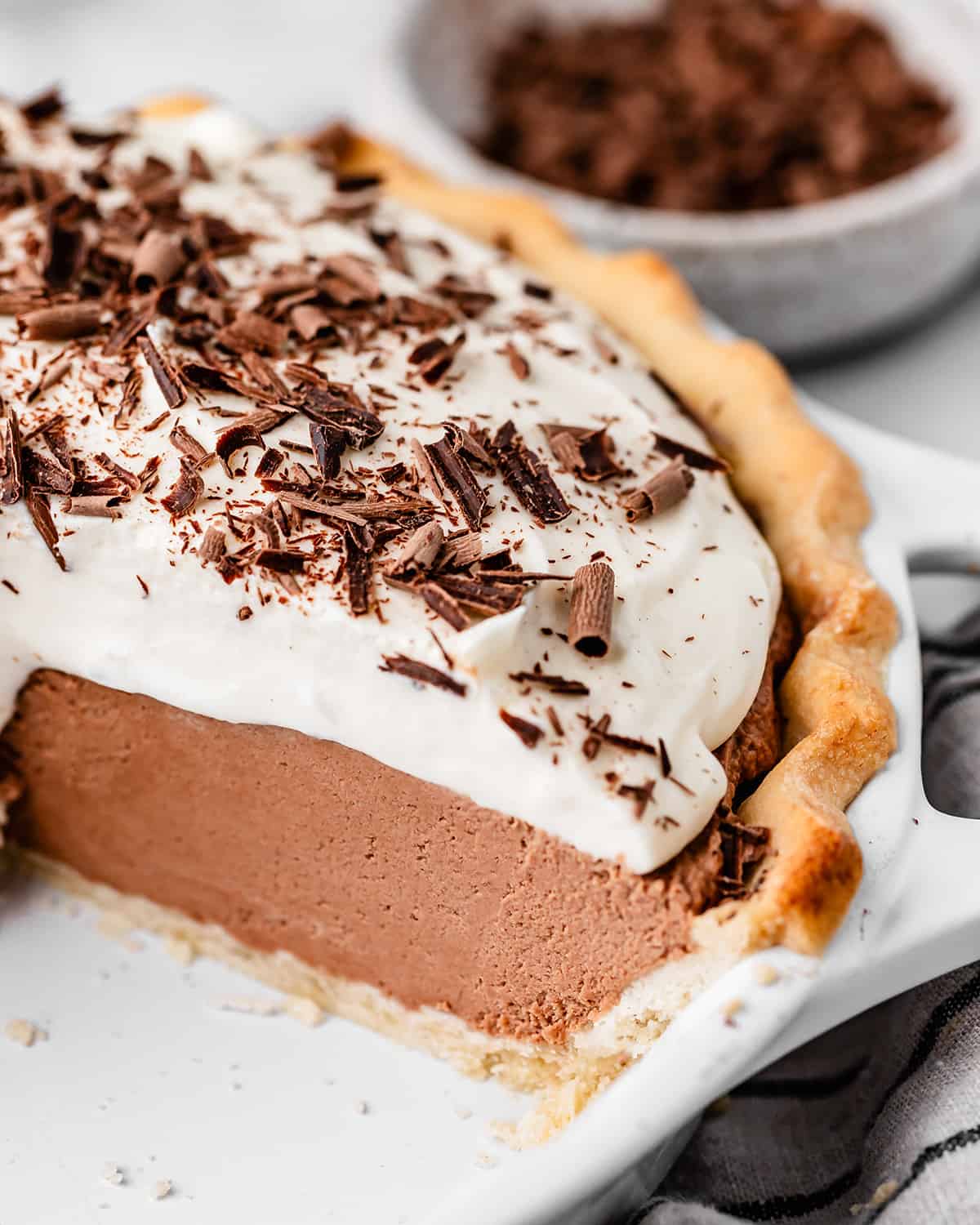 In this Homemade French Silk Pie recipe, a flaky pie crust is filled with a chocolate cream filling and topped with homemade whipped cream! This chocolate silk pie recipe is made from scratch and tastes even better than Baker's Square or Village Inn! #frenchsilkpie #frenchsilk #chocolatesilk french silk pie in a pie dish with a piece cut out of it