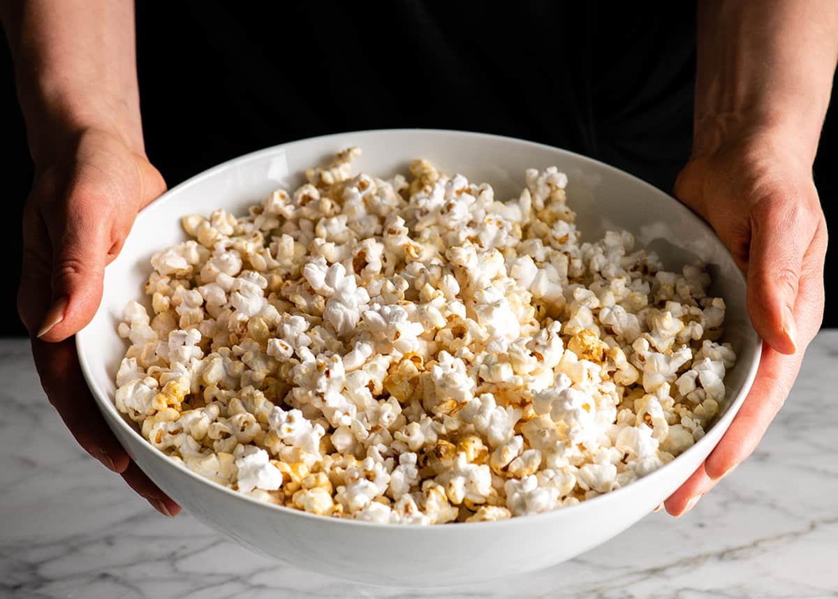This easy homemade Kettle Corn Recipe is made with 4 ingredients, in less than 5 minutes on the stovetop. Better than the kettle corn at the fair! It's gluten-free and dairy-free! Front view of someone holding a large bowl of homemade kettle corn