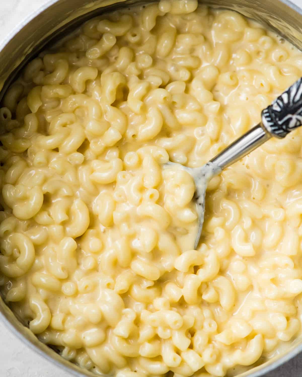 This Easy Homemade Mac and Cheese Recipe is made with 8 ingredients in 15 minutes on the stovetop (no baking required)! Time to ditch the boxed mac and cheese for this irresistibly creamy, smooth & cheesy homemade recipe! #homemade #macandcheese #homemademacandcheese #sidedish #maindish #kidfriendly overhead photo of homemade mac and cheese in a pot with a spoon taking a scoop