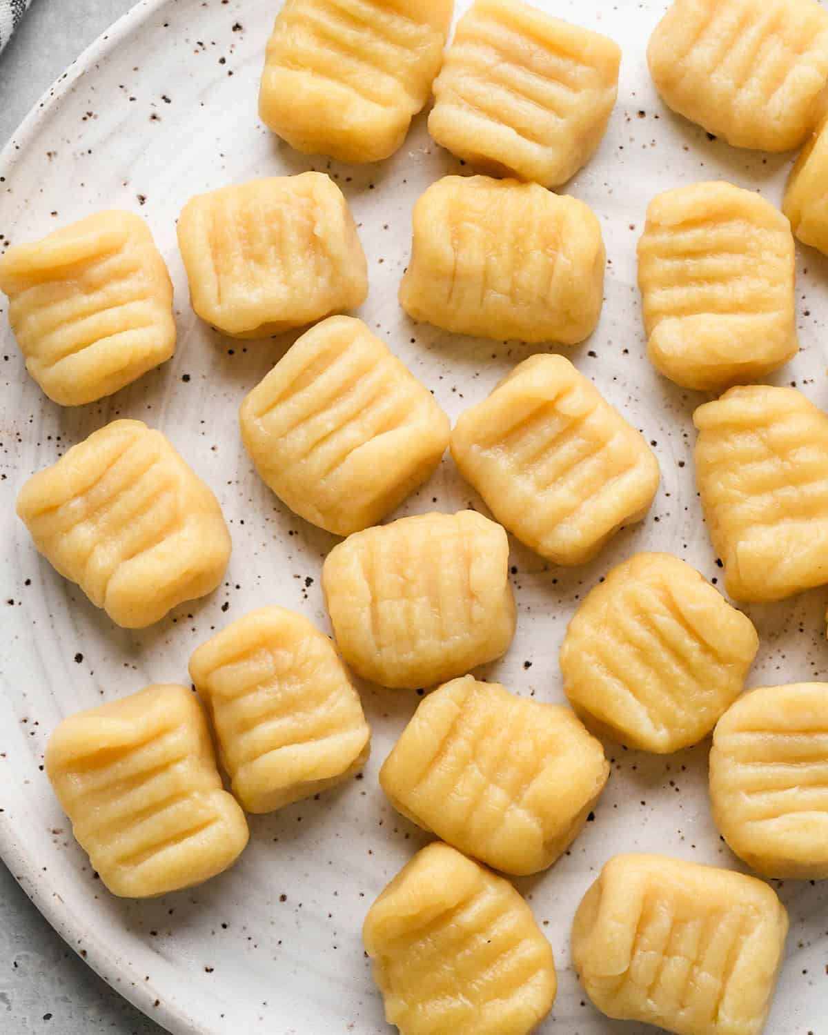 This Homemade Potato Gnocchi Recipe is made with only 5 ingredients and is SO much better than store bought varieties! Seriously we only ever eat homemade gnocchi! This version has cheddar cheese in the dough, setting it apart from all the others! It’s freezer friendly and beloved by kids and adults! #gnocchi #recipe #homemade #potatognocchi #fromscratch #healthyrecipe boiled Potato Gnocchi on a plate