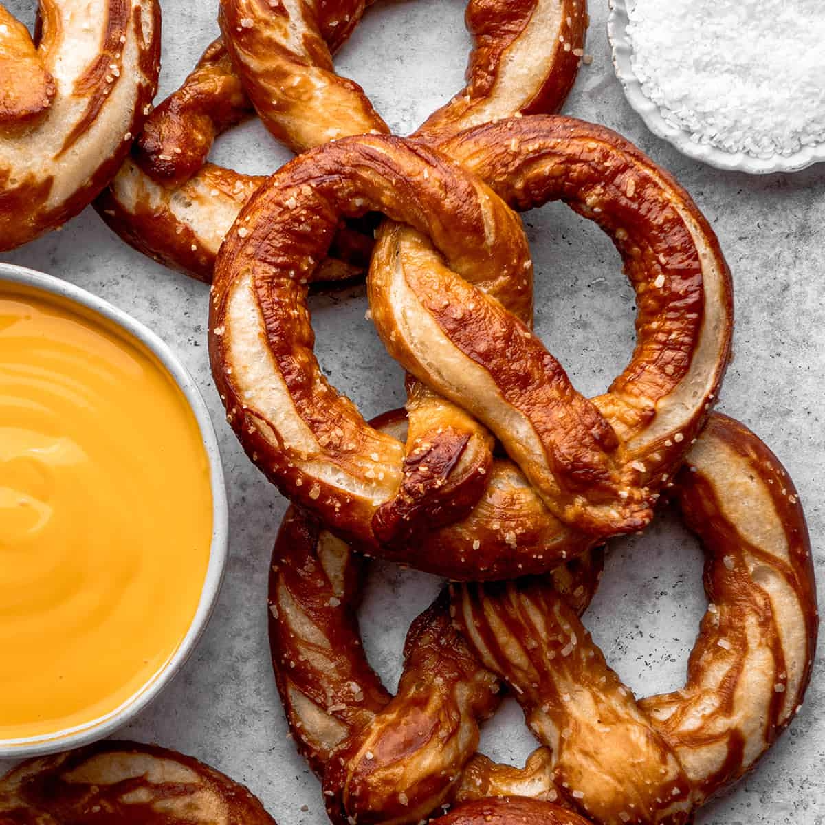 overhead view of four homemade soft pretzels with salt and cheese sauce on the side