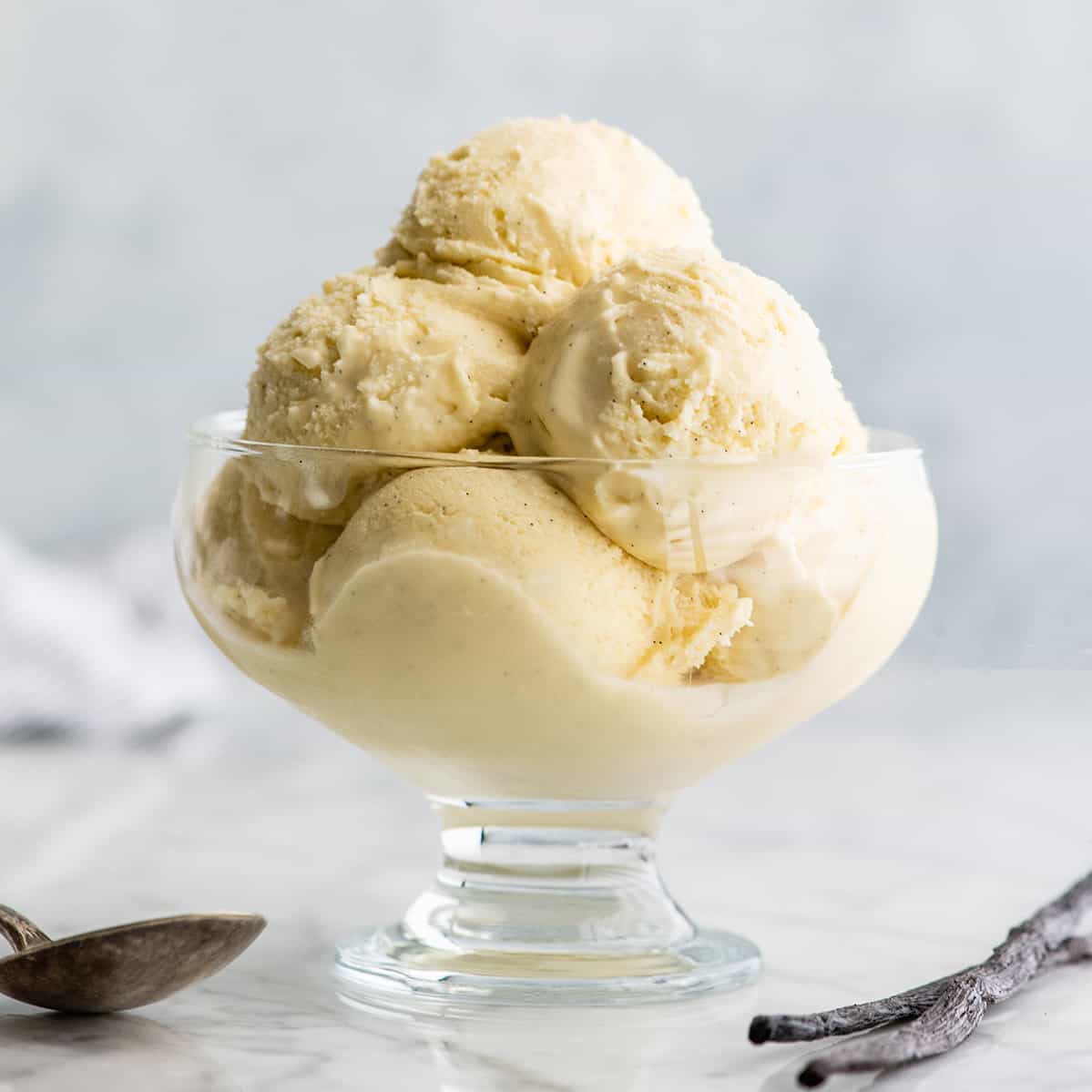 This homemade vanilla ice cream recipe is rich and creamy with a deep vanilla flavor. Watch the video and follow our step-by-step instructions to learn how to make this 5-ingredient vanilla bean ice cream recipe! front view of a glass dish with scoops of vanilla ice cream inside