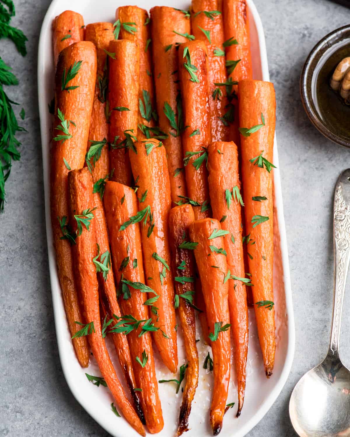 Honey Roasted Carrots are an addicting vegetable side dish perfect for any occasion! This honey carrots recipe only has 5, good-for-you ingredients and is super easy to make! Overhead view of honey roasted carrots on an oval platter sprinkled with carrot greens